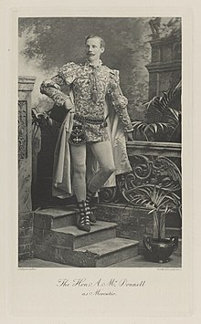 Black-and-white photograph of a standing man with a mustache richly dressed in an historical costume