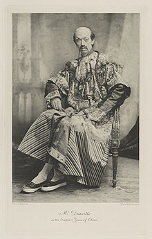 Racist black-and-white photograph of a seated man richly dressed in an historical costume apparently from China