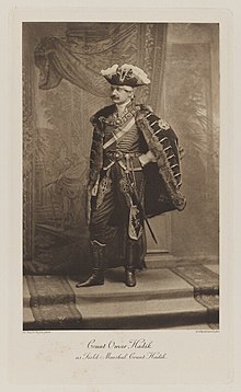 Black-and-white photograph of a standing woman richly dressed in a historical military costume