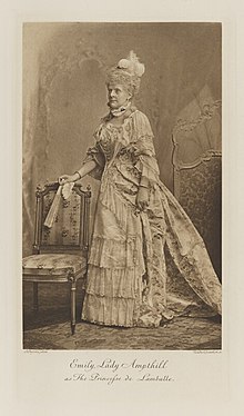 Black-and-white photograph of a standing woman richly dressed in an historical costume