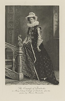 Black-and-white photograph of a standing woman richly dressed in an historical costume