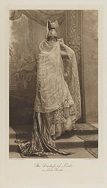 Black-and-white photograph of a standing woman richly dressed in an historical costume that is supposed to look Turkish or Persian but is just a costume