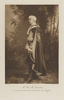 Black-and-white photograph of a standing man richly dressed in an historical costume with a long cloak and a tri-corner hat