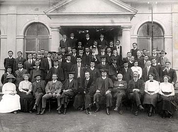 Studente en personeel van die Voorbereidende en Teologiese Skool op Potchefstroom voor die eerste gebou, 1913. Voor: Hester Coetzee, Betsie Postma, S.G Yssel, J.J.A. Coetzee, prof. Ferdinand Postma, prof. J.D. du Toit (Totius), prof. A.P.C. Duvenage, prof. Jan Kamp, Piet van der Walt, Rachel Wentzel, Vera Gill. Tweede ry: Nollie Vermaas, G.P. van der Linde, J.V. Coetzee, Douw Venter, C.J.H. de Wet, J.C. van der Walt, D.N. Kotzé, H.F. Duvenage, Vera Pienaar, Frikkie Potgieter, J.L.M. Wiechers. Derde ry: Piet Coetzee, Jan Triechaardt, Nic Steyn, B.J. de Klerk, J.H Boneschans, H.S. van Jaarsveld, Pieter Coetzee. Vierde ry: Prof. Joon van Rooy, ene Oosthuizen, C.W.M. Du Toit, E.L.J. Venter, T.D. Venter, Daan Marais, J.V. Coetzee, Lou van Rooy, A.S.E. Yssel, H. van der Walt, S.P. Engelbrecht, Izak le Roux, ene Marais, L.J. du Plessis. Vyfde ry: ene Scholtemeyer, Willie Geere.