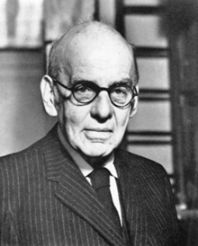 Photograph of a bald man wearing a suit and glasses