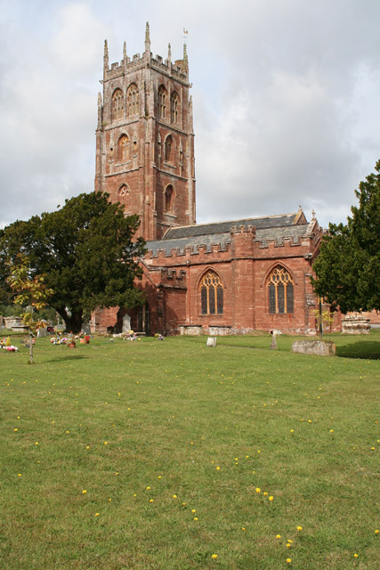 Red stone building with square tower. In the foreground is a graveyard.