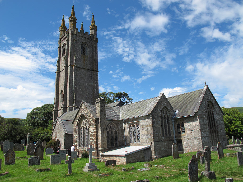 Grey stone church and huge bell tower with grave stones in front.