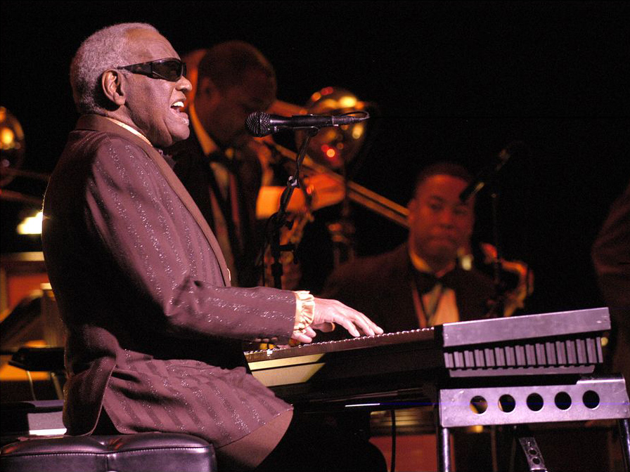 How to play blues piano. Man in suit and black sunglasses playing keyboard on stage.