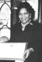 An African-American woman, smiling, holding an award plaque. She is wearing a dark business suit.