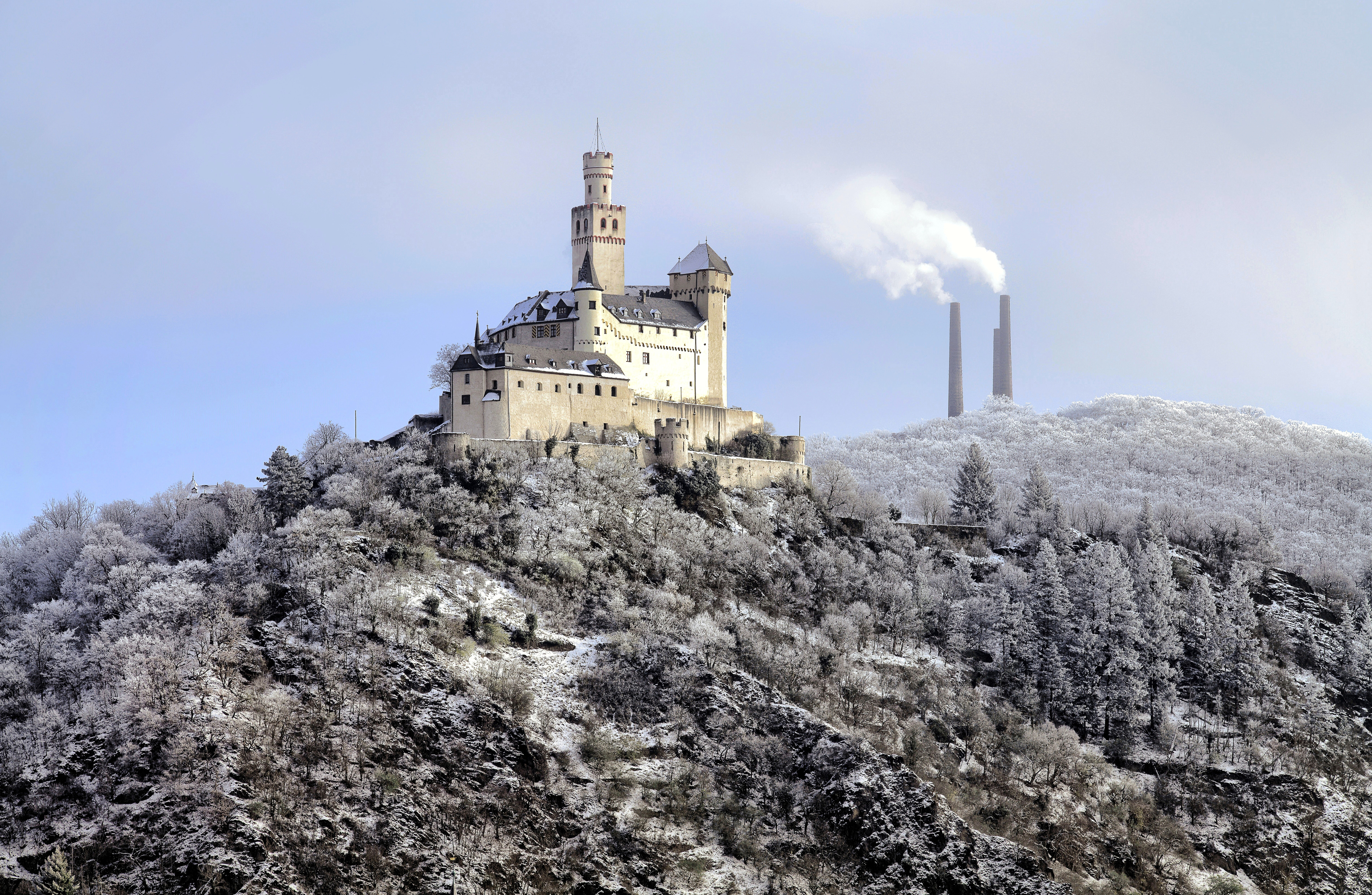 Marksburg Castle in winter, with the striking chimneys of the Braubach lead and silver smelter, one of the oldest industrial monuments in the Middle Rhine region, to the right.