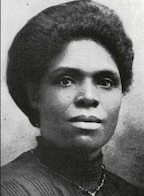 The face of an African-American woman with dark skin and hair; her hair is dressed in a bouffant updo, away from her face. She is wearing a dark dress.