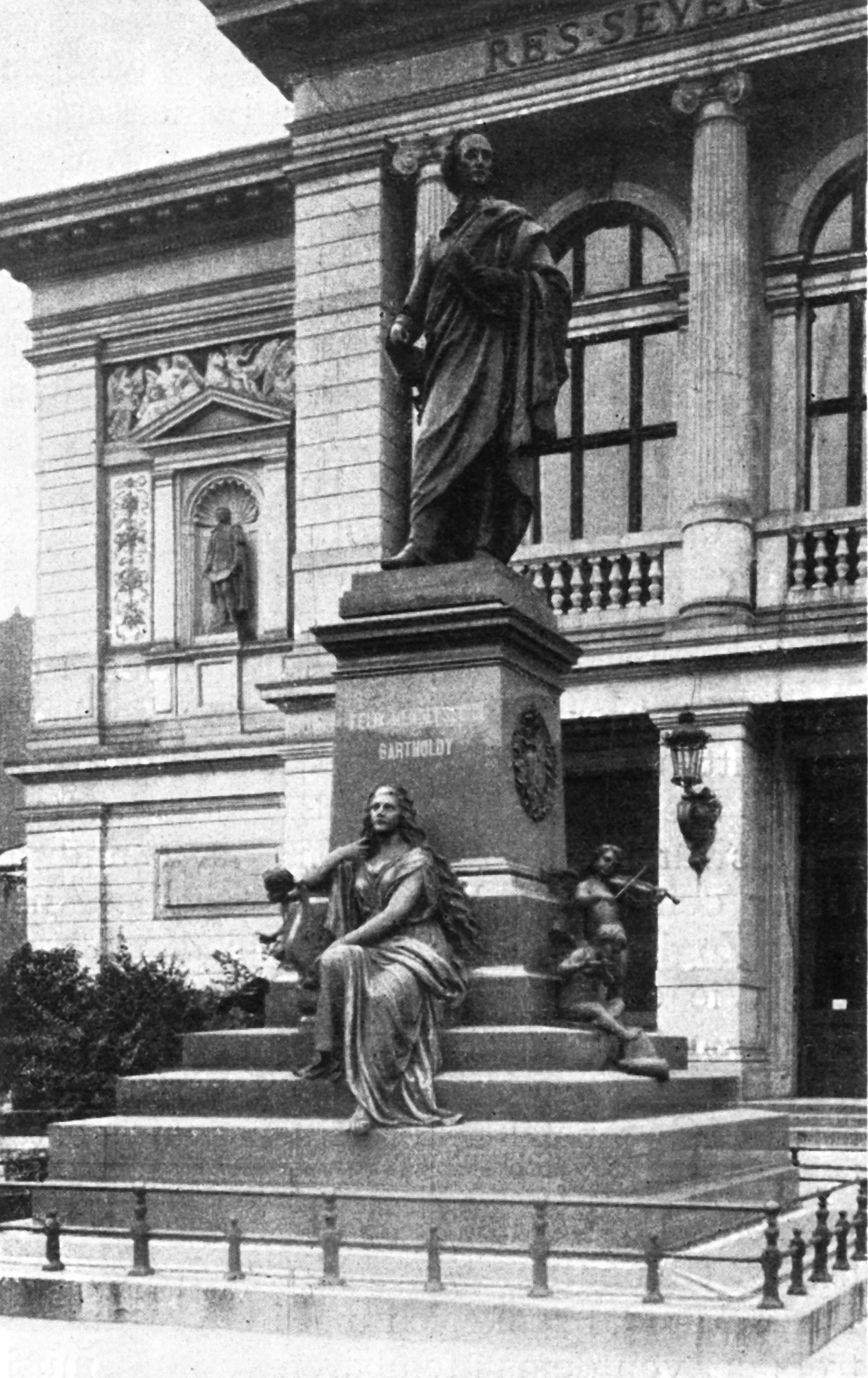 чёрно-белая фотография статуи облачённой мужской фигуры на ступенчатом постаменте, с выграавированнной надписью «Феликс Мендельсон Бартольди», с сидящей женской фигурой, держащей лиру на его основании, напротив арочной здания