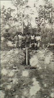 Soldiers digging up a long pipe like object that has been planted in the middle of a road.