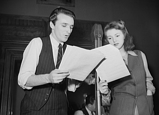 Rehearsal for the World War II radio show You Can't Do Business with Hitler with John Flynn and Virginia Moore. This series of programs, broadcast at least once weekly by more than 790 radio stations in the United States, was written and produced by the radio section of the Office of War Information (OWI).