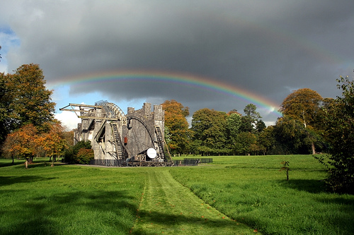 The Leviathan of Parsonstown Telescope with a double rainbow in the sky overhead and trees at either side and in the background of the image