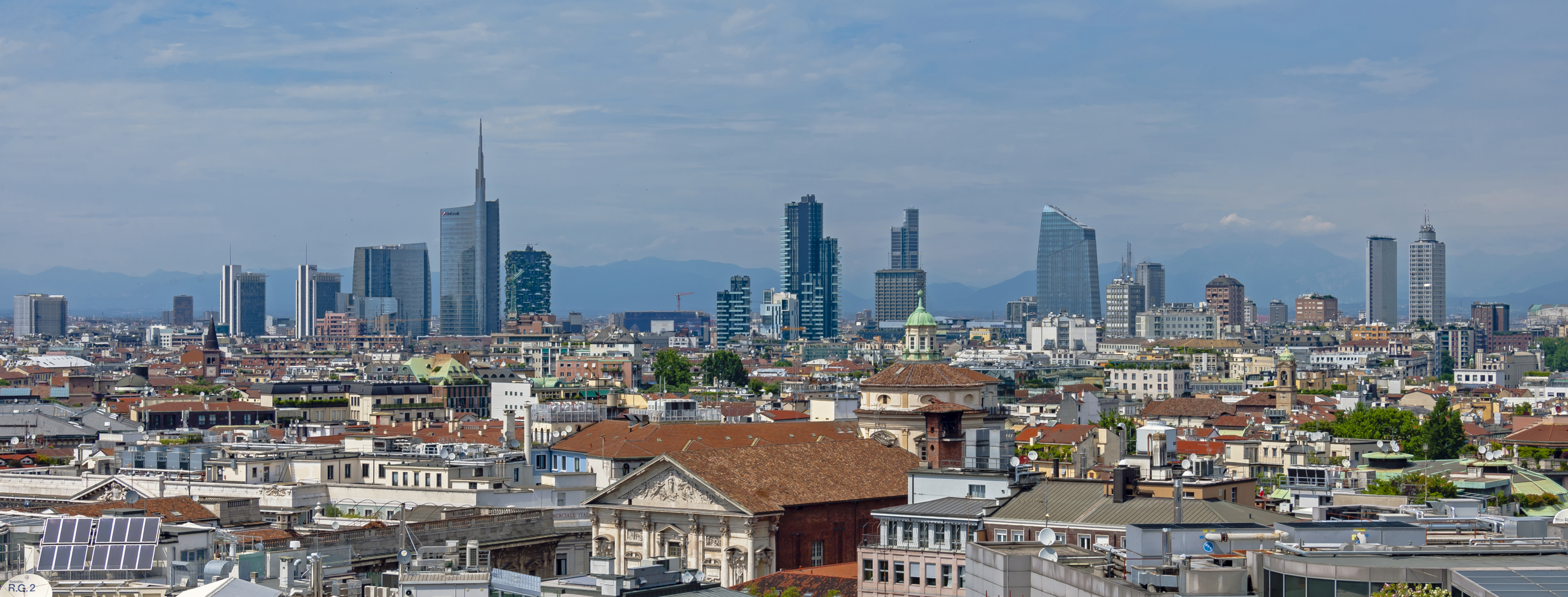 [Image: Wide_angle_Milan_skyline_from_Duomo_roof.jpg]