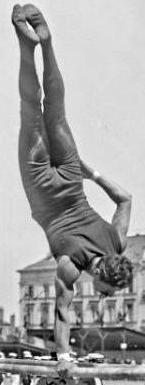 Black and white photo of an upside down man with one hand on a bar and his other hand on his leg