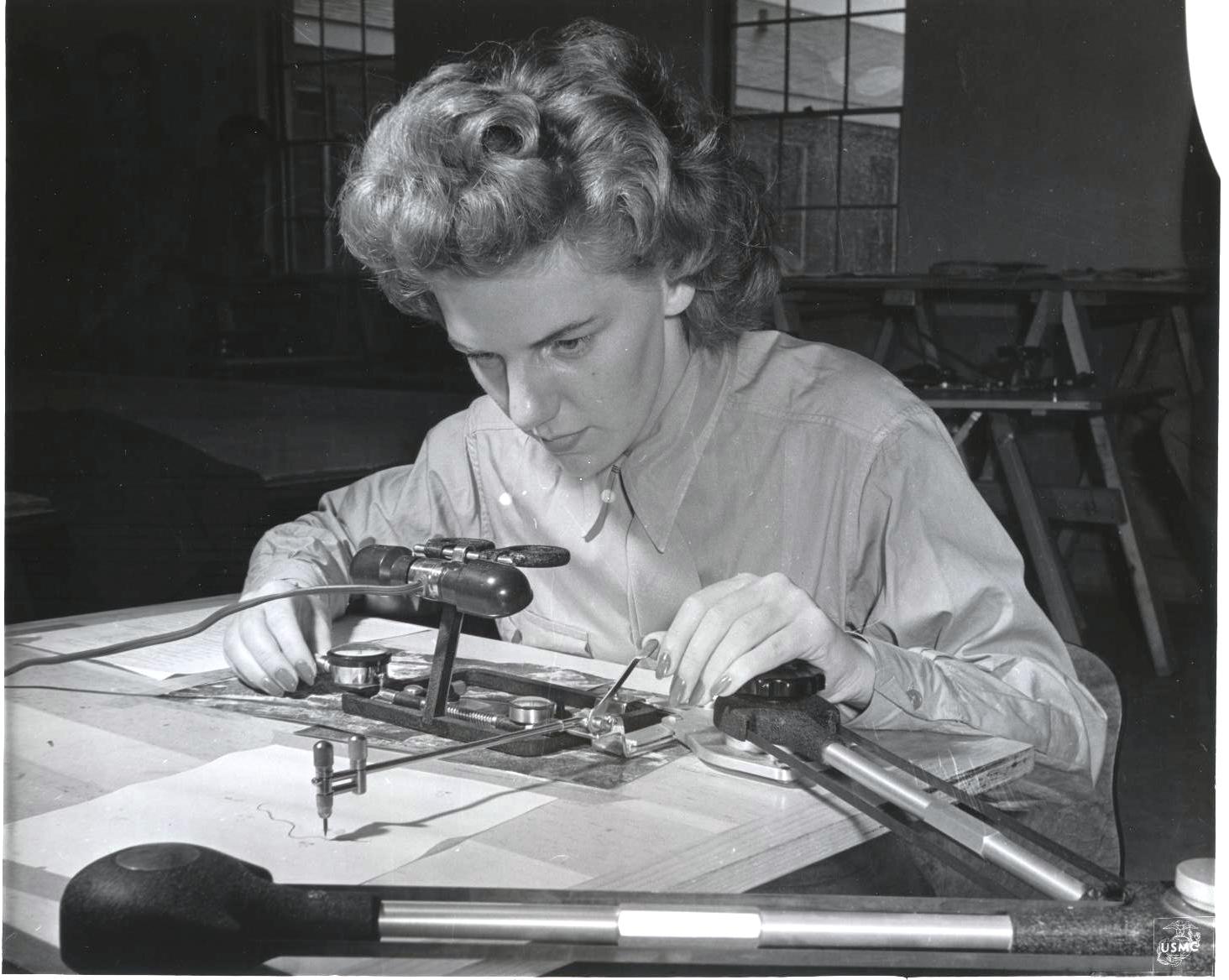 A person is seen on a desk using a contour finder to delineate a map from an photograph.