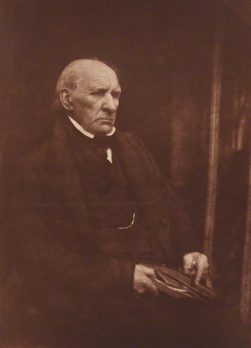 a photograph of an old man with grey hair wearing a suit with the chain of a pocket watch visible 