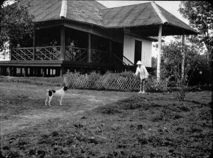 File:COLLECTIE TROPENMUSEUM Man en hondje voor het huis op een rubberonderneming Oost-Sumatra. TMnr 60005380.jpg