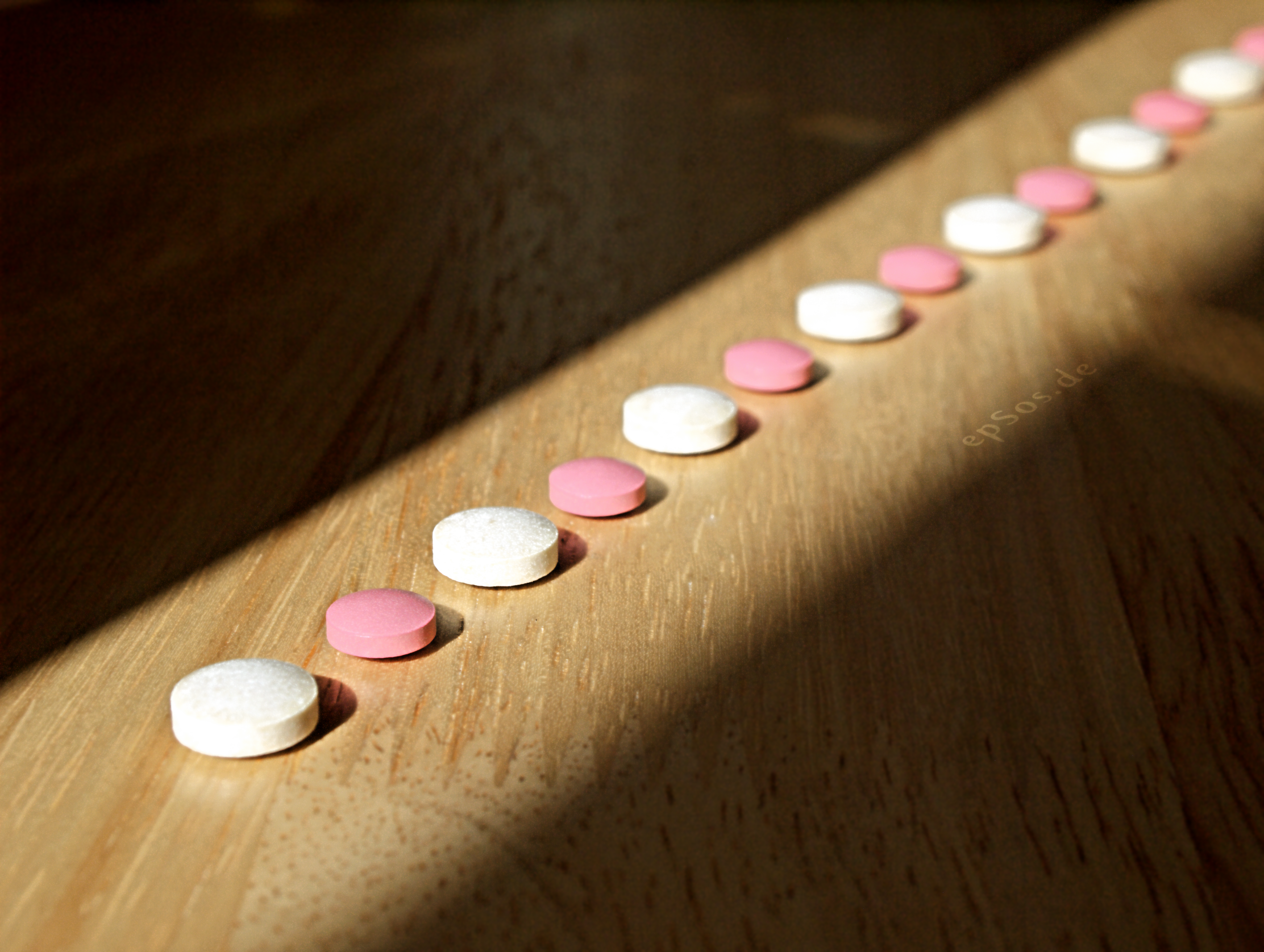 Pink and white pills lined up in a beam of light