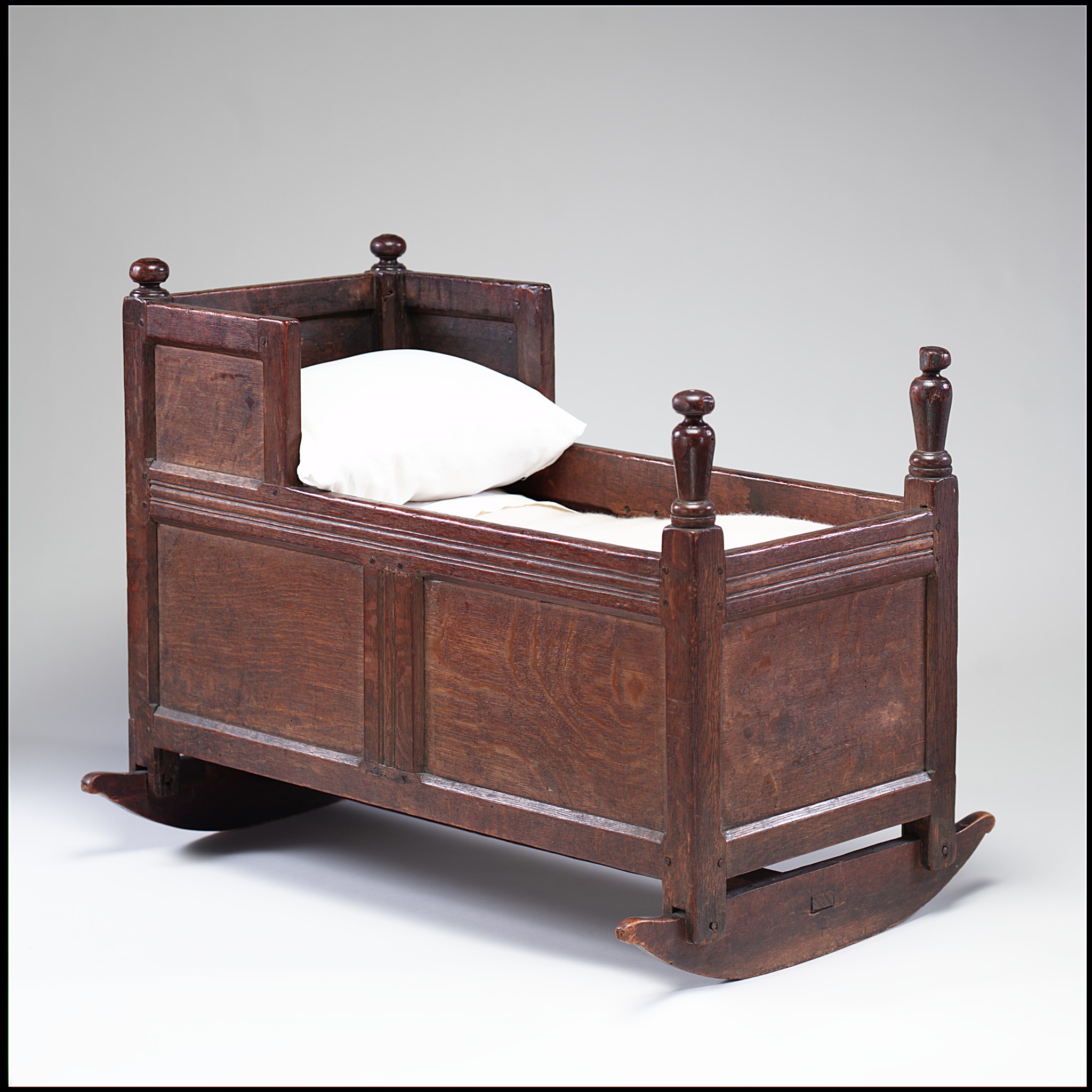 An image of an antique American cradle with solid wooden sides and a white pillow.
