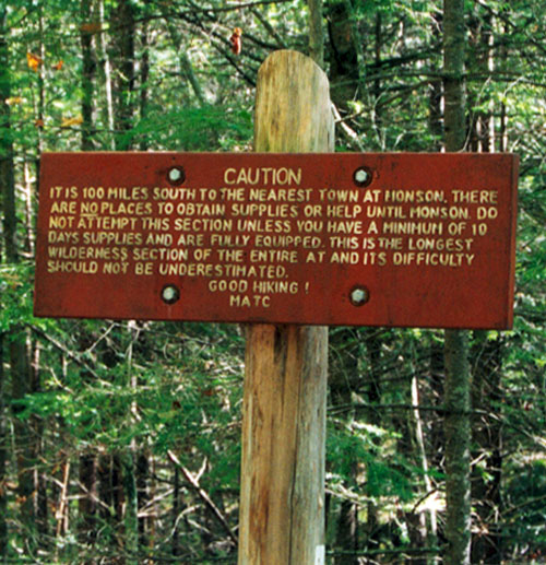 Wooden sign reading "Caution. It is 100 miles south to the nearest town at Monson. There are no places to obtain supplies or help until Monson. Do not attempt this section unless you have a minimum of 10 days supplies and are fully equipped. This is the longest wilderness section of the entire AT and its difficulty should not be underestimated. Good hiking! MATC"
