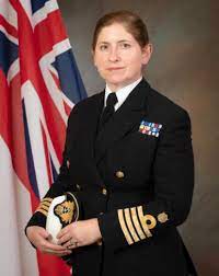 An official image of Catherine Jordan when she was a Captain, in dress uniform and standing in front of a draped flag of the United Kingdom