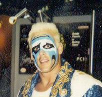 A headshot photograph of a blonde man wearing blue, black and white facepaint