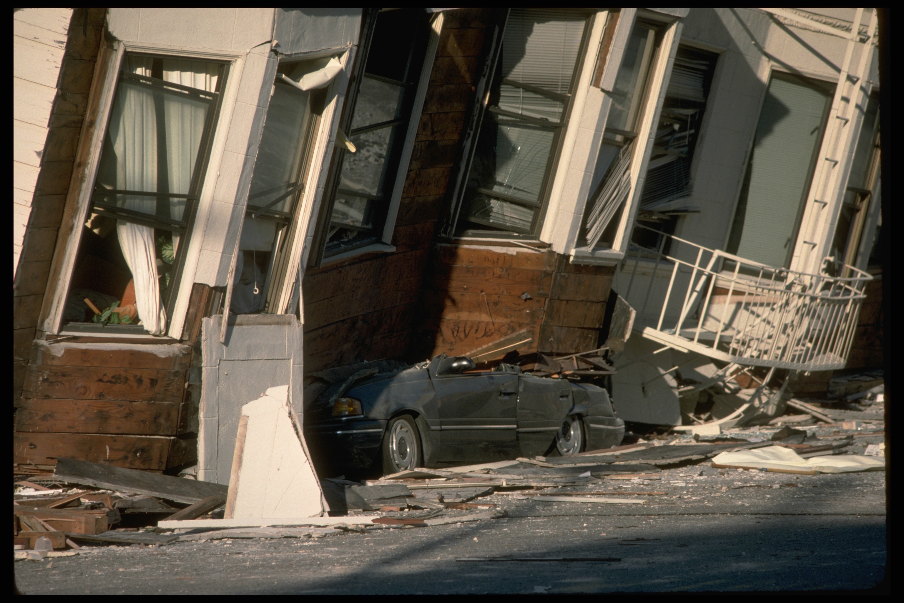 A house has been so badly damaged by an earthquake it is tilting over onto a car in the street.