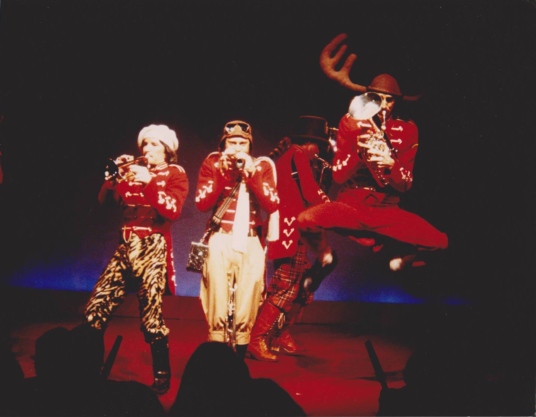 The Brass Band performing live at The Last Laugh in Melbourne, Australia. Buford is captured mid-jump while Frumheimer prances around behind him, Jimby, and Loois.  