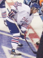 Photographie en couleur d'un joueur de hockey sur la glace avec un maillot blanc et un casque bleu