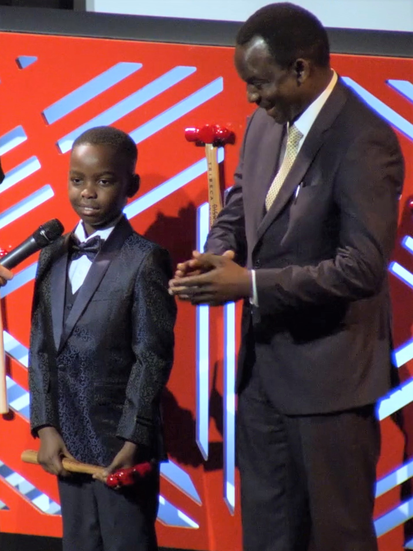 Adewumi (left), receiving 2019 Tribeca Disruptive Innovation award as his father applauds