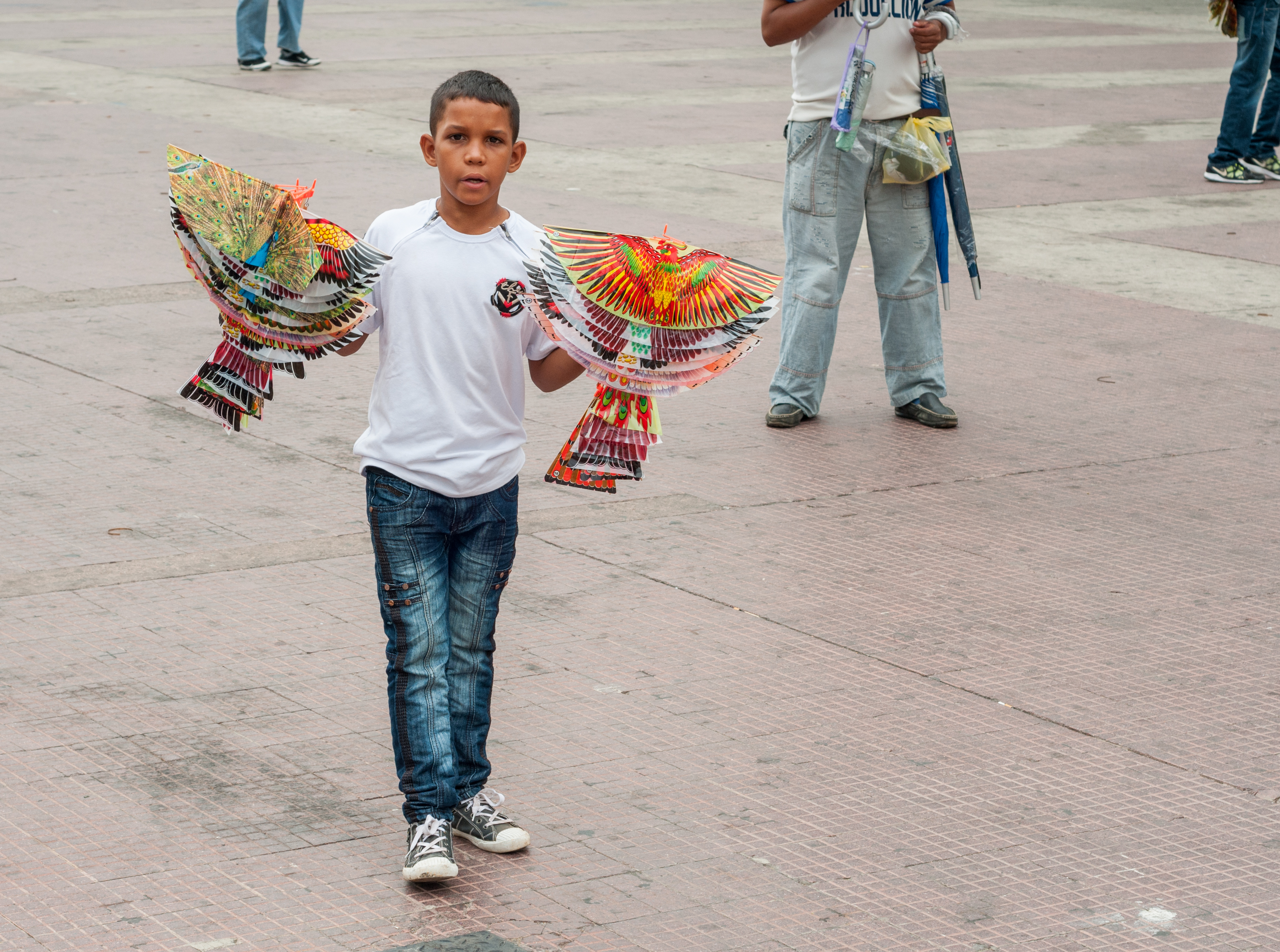 A young boy in jeans and a white T-shirt holding two colorful handfuls of brightly colored toys