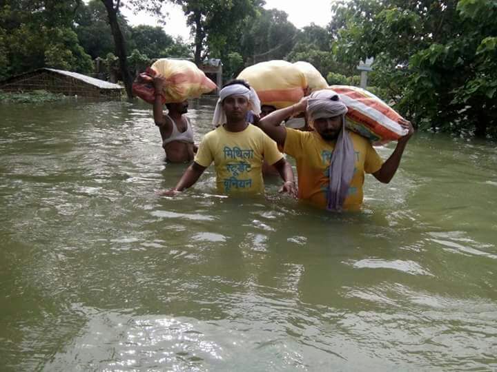 Four men wading through waist-high waters carrying huge sacks over their heads.