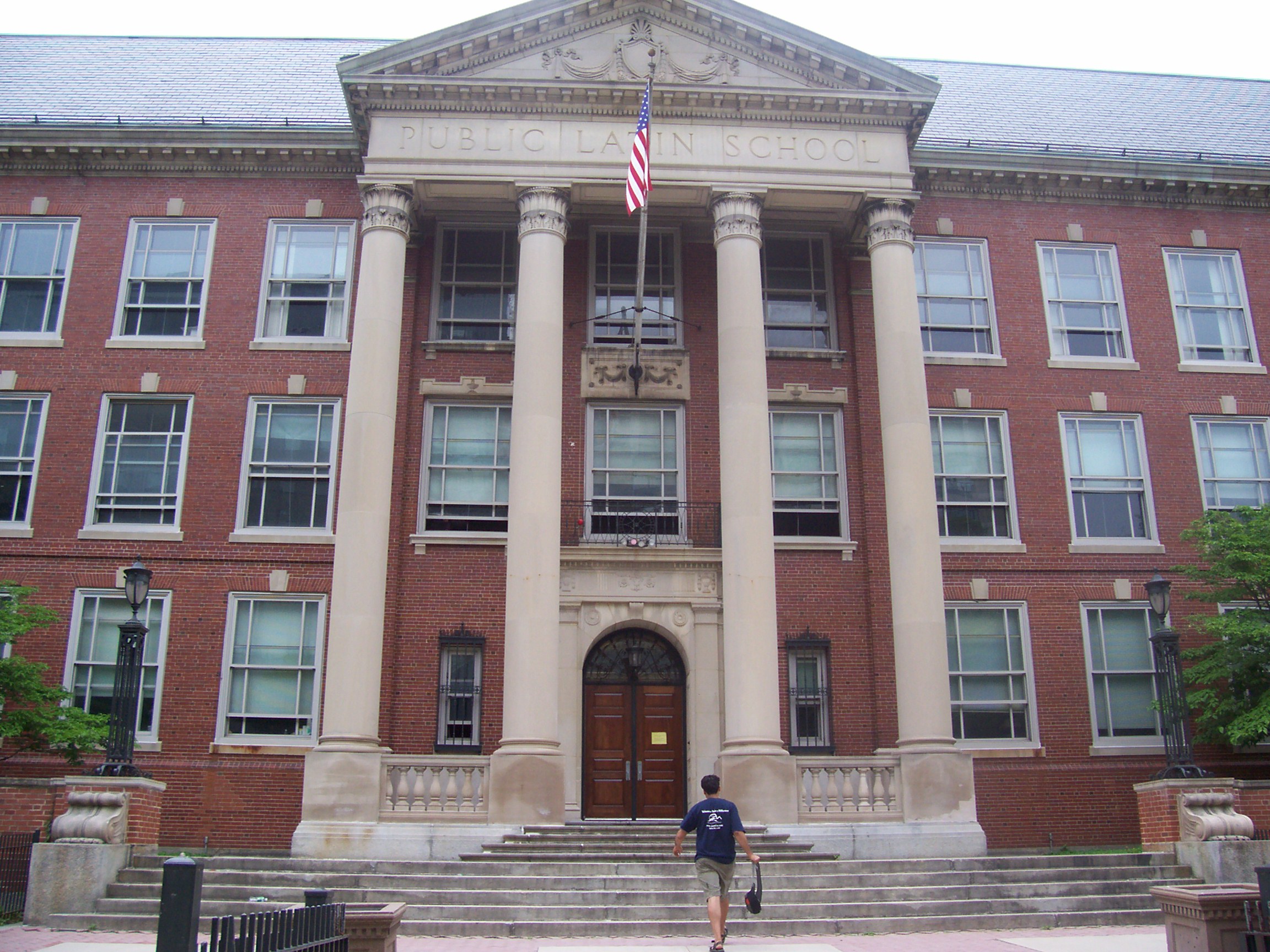 A photograph of the entrance to a building displaying three stories of windows, a four-column portico, and a sign reading "BOSTON LATIN SCHOOL".