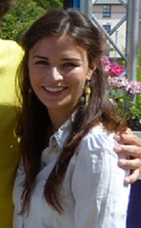A white woman with long hair, wearing white shirt is smiling at the camera. There is an arm around her but the person is cropped out.