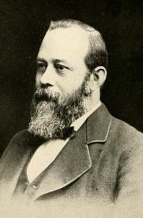 An older white man with a receding hairline and a greying beard; he is wearing a suit and a bowtie.
