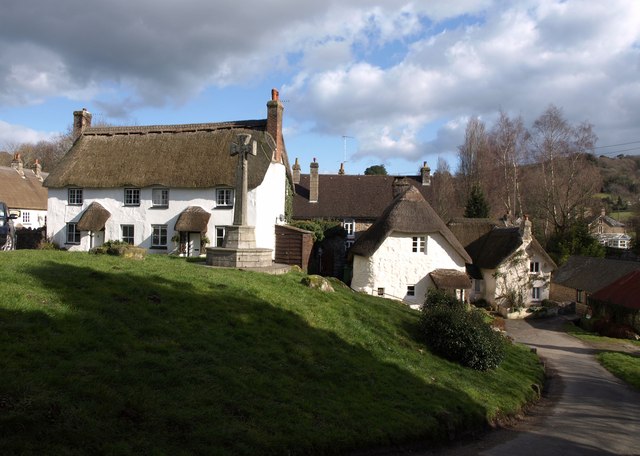 Thatched Devon cottages behind grassy mound with a large stone cross.