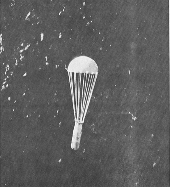 A parachute with a canister hanging below it dropping over the sea