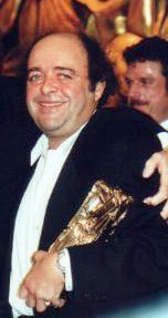 Un homme souriant tenant dans son bras un César, statuette dorée.