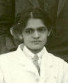 An Indian woman's face; she is wearing a white doctor's coat. Her dark hair is parted center and pinned up.