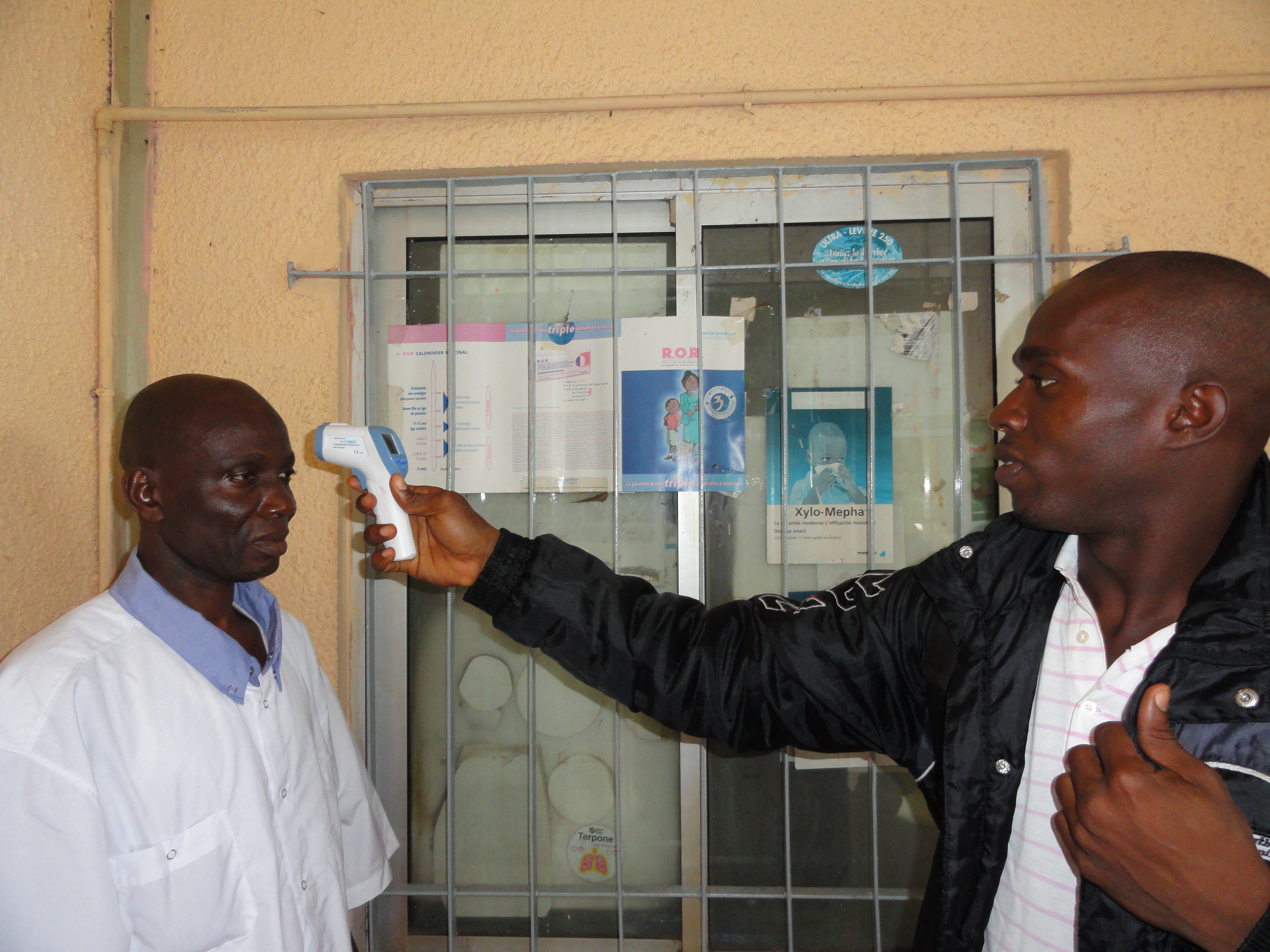 A person points a hand-held, non-contact thermometer at the forehead of another person.