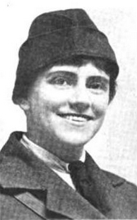 A smiling white woman wearing a uniform-style cap and coat, over a collared shirt and necktie