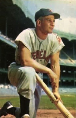 Baseball player Al Rosen, a 29-year-old blond man, is pictured in the white uniform of the Cleveland Indians, kneeling with a baseball bat, circa 1953.
