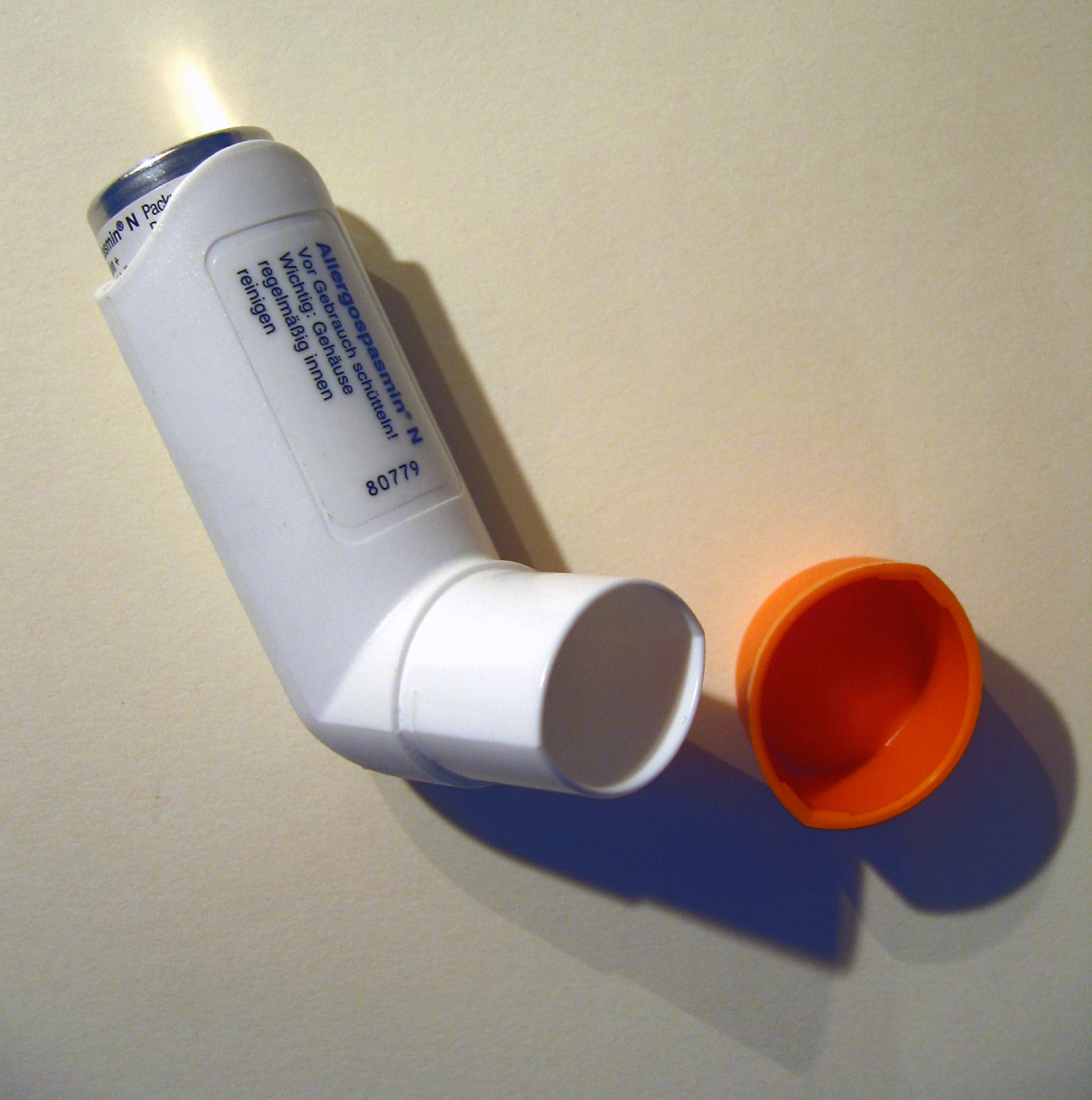 White inhaler on a table with orange cap next to it.