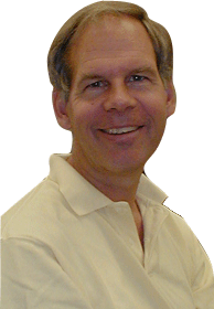 Usměvavý bělošský muž středního věku na sobě světle žluté polo tričko rozepnuté na límci.