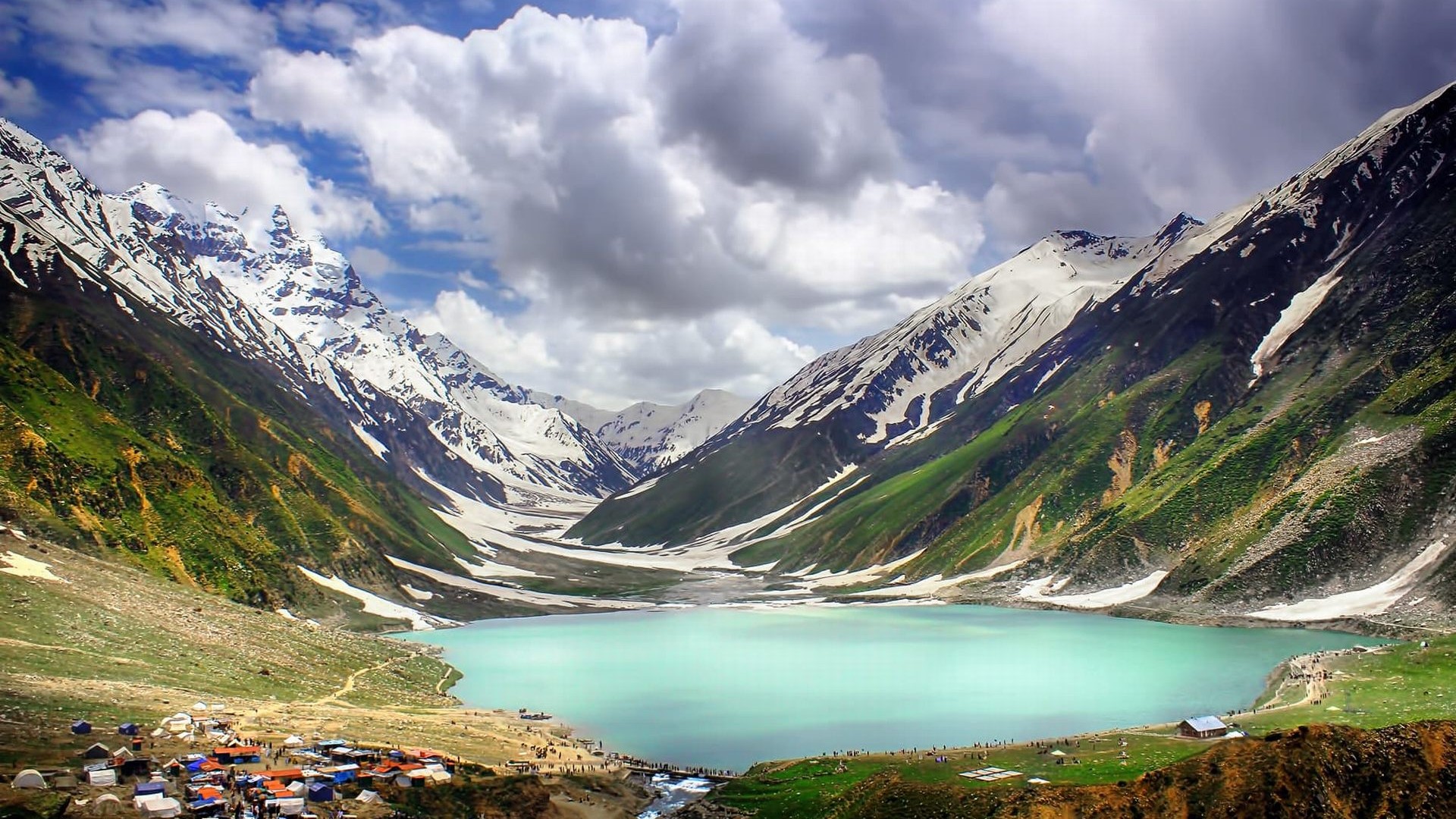 Light blue lake with snow capped mountains infront of it on a cloudy day