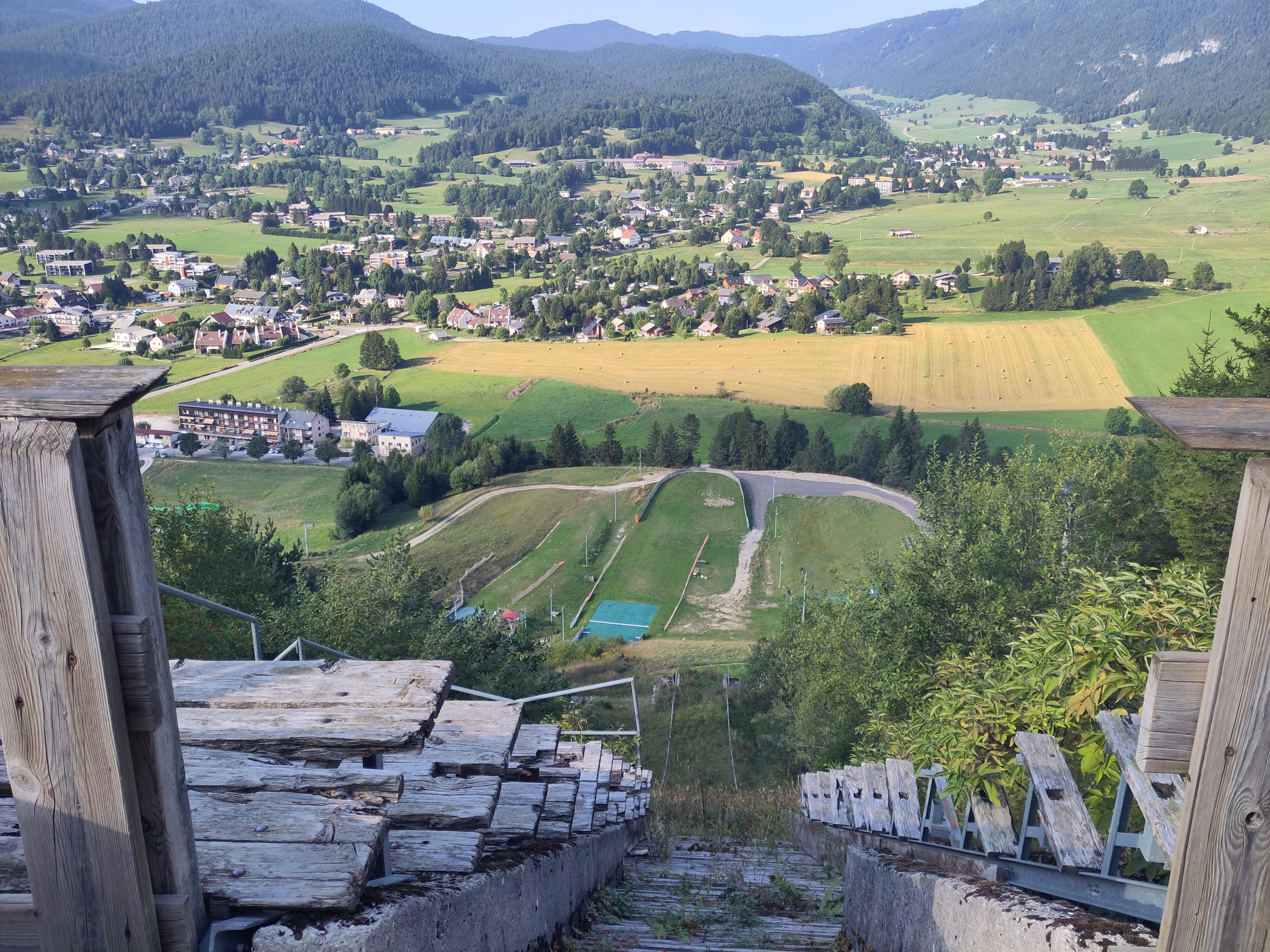 Vue depuis le haut du grand tremplin de saut à ski, en bois et abandonné. La végétation a repris ses droits. En face, le village dans les collines.