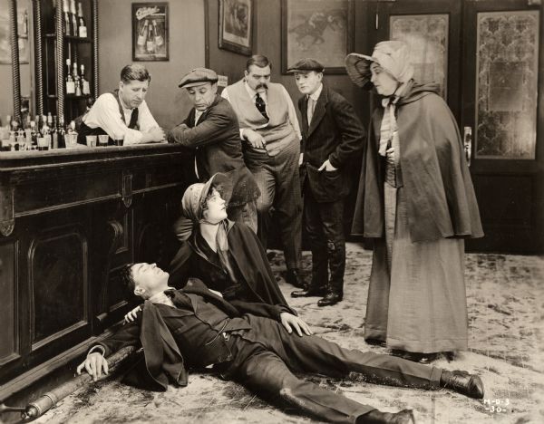  Jack Bronson (played by Raymond Bloomer) has been beaten senseless in an underworld bar. Violet Gray (played by Marion Davies dressed in a Salvation Army uniform) kneels beside him to offer aid in a scene still from the 1919 silent drama The Belle of New York (1919).